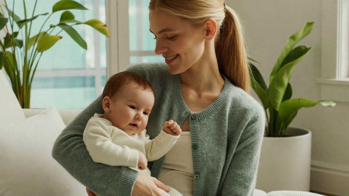 Jeune maman assise en douceur pres d'une fenetre lumineuse, main posee sur le ventre, interieur parisien epure