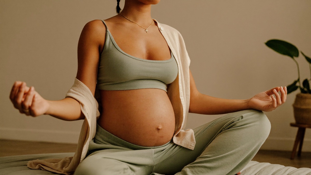 Femme enceinte assise sereinement pres d'une fenetre, lumiere naturelle, preparation douce a l'accouchement